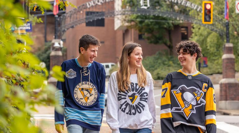 Duquesne students walking on campus in Pens gear.