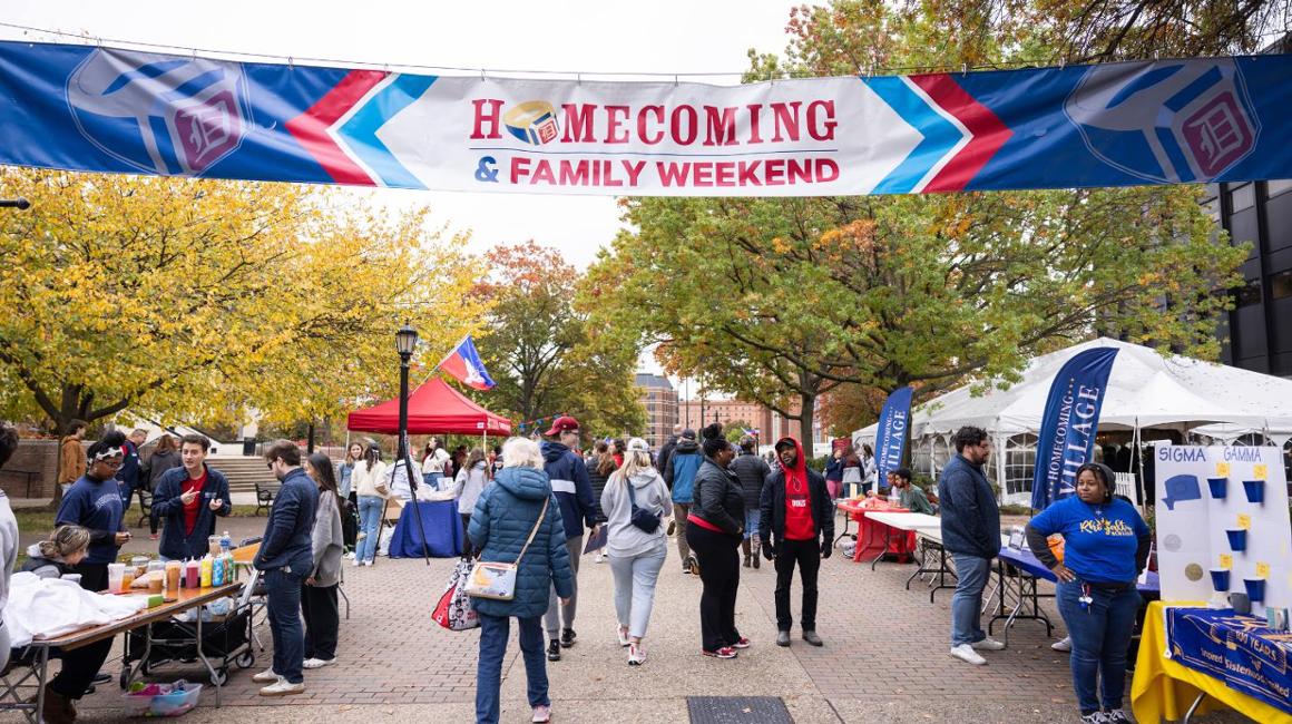 people walking on Academic Walk on Duquesne University's campus under a banner that says Homecoming and Family Weekend