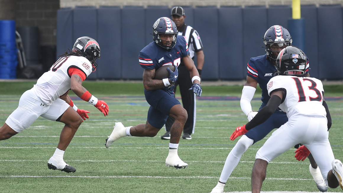 Four football players running, one carries the ball