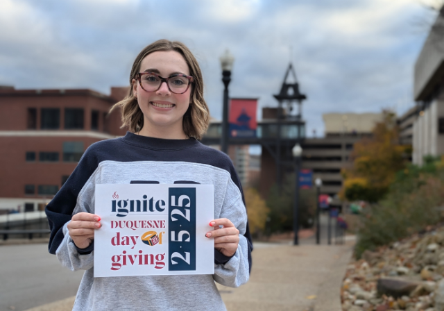 Female student holding up a 2025 day of giving sign