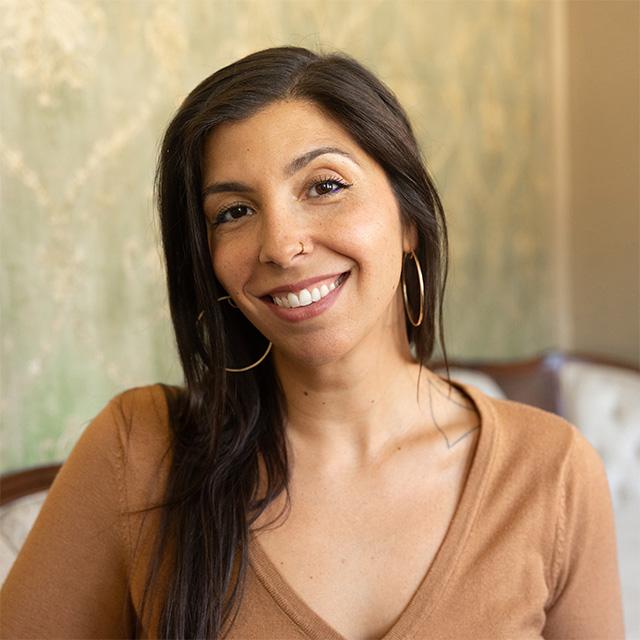 A person poses for a photo in front of a beige background.