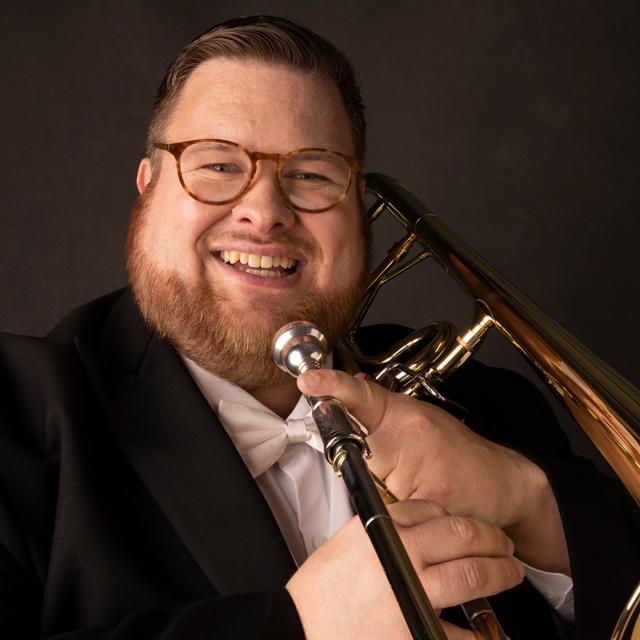 man wears a tuxedo and holds a trombone