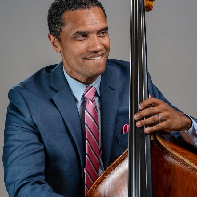 Paul Thompson plays upright bass in front of a gray background.