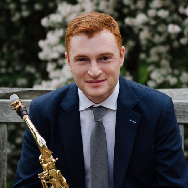 Person sitting with saxophone in front of flowers