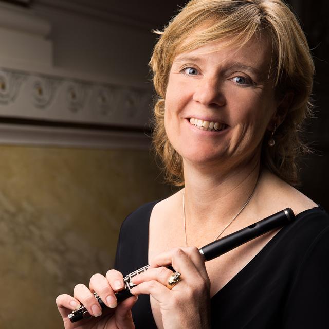 Rhian Kenny holds a piccolo in front of a dark elegant background.