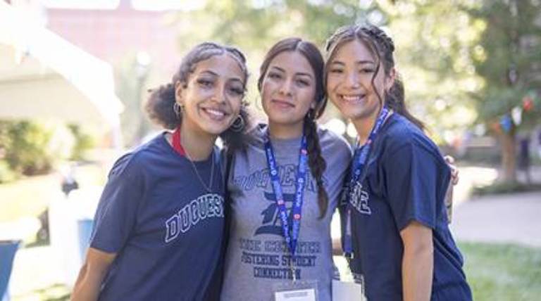 Three girls stand smiling on a sunny day
