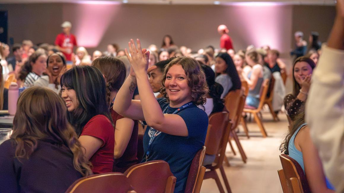 A student clapping her hands at Orientation 2026 with a room full of first-year students.