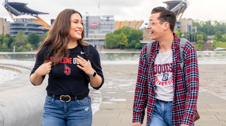 Two students wearing Duquesne shirts smile and laugh while walking