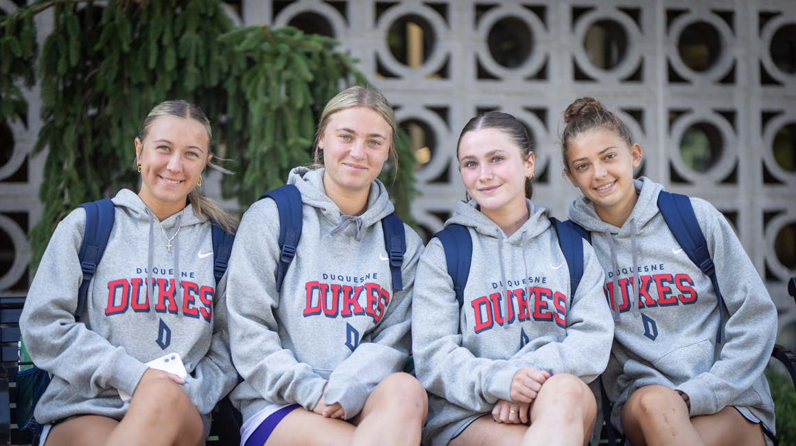 Four Duquesne students sit together wearing Duquesne Dukes hoodies.