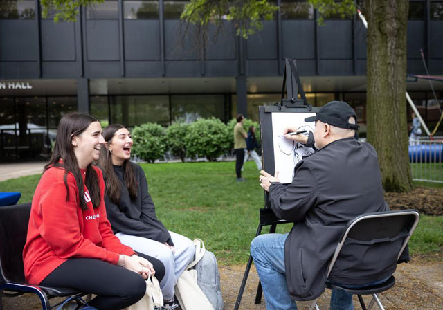 Two students laugh as an artist draws their caricatures during the Festival on the Bluff on campus.