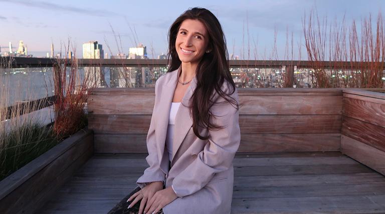 Giovanna Elo sits on a rooftop against the New York City skyline