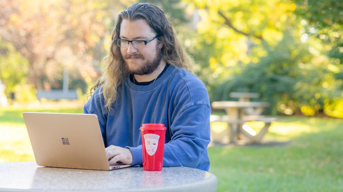 Deagan Moore sits at a table outdoors and studies on his laptop