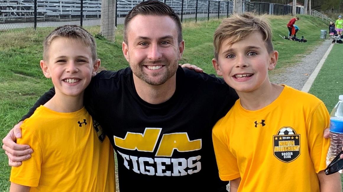 Principal Matt Heckman stands outdoors with two young students