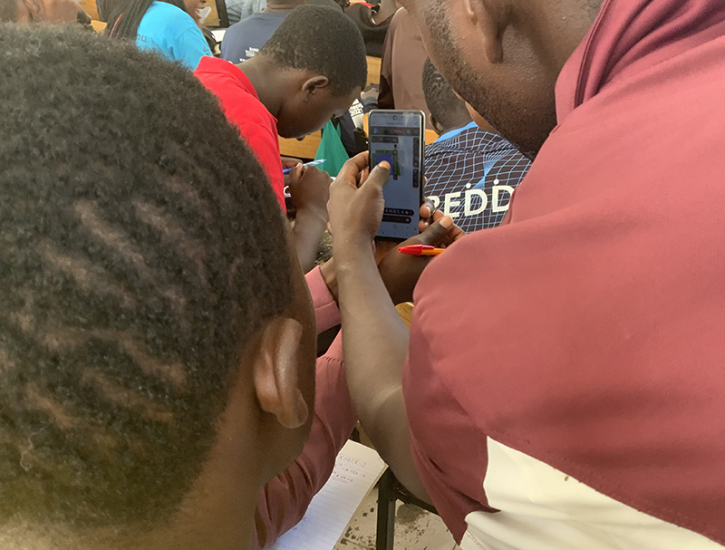 Students gather around a cell phone to view classroom discussion topics on the screen