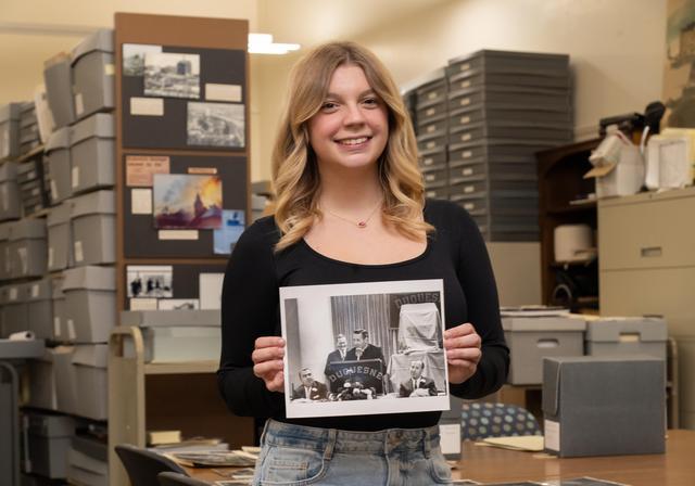 Riley Adams stands in University archives and holds a photo of her great-grandfather Vernon Gallagher