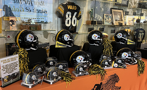 Pittsburgh Steelers helmets, jerseys and memorabilia are displayed on a table covered in an orange tablecloth at the Shazier Fund annual event.