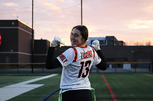 Viv stands on a football field wearing her flag football team's jersey