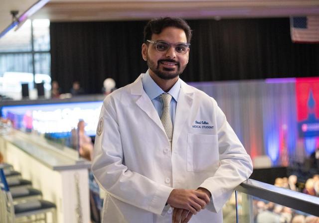 Medical student Abbad Sultan stands against a railing wearing his white coat.