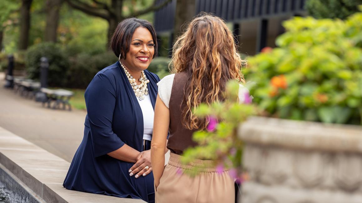 Dean Gretchen Generett sits on the edge of the fountain with a student