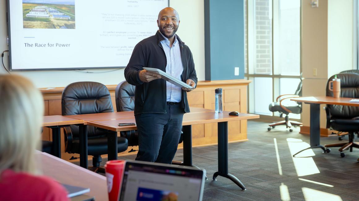 Dr. Kevin Henderson stands in front of a classroom leading a discussion. 