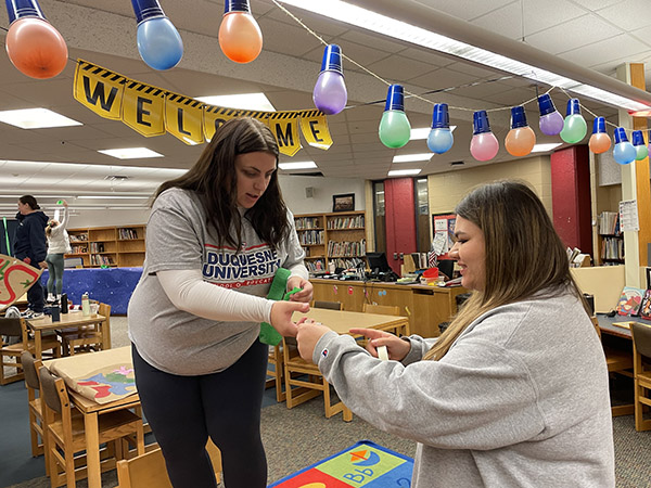 School of Education Ambassadors Kate Atkins and Kenzie Bole hang holiday decorations in preparation for the celebration