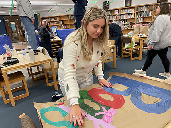 School of Education Ambassador Zoe Brunick prepares to hang a hand-painted holiday sign in the Pittsburgh King Pre-K-8 library