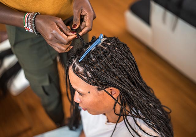 A woman braiding a black lady's hair